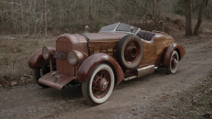 An old roadster-style car sits on a dirt road