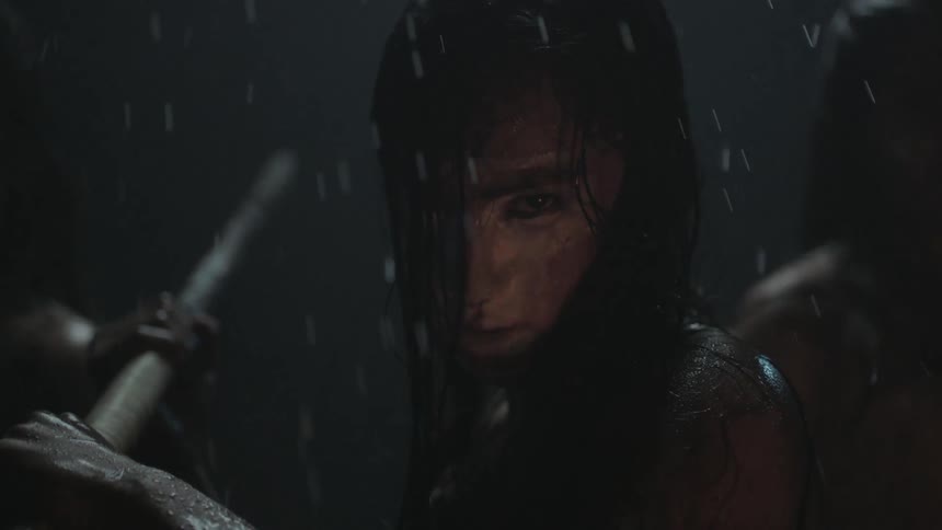 A woman adapts an attack pose while holding a large stick on a rainy night