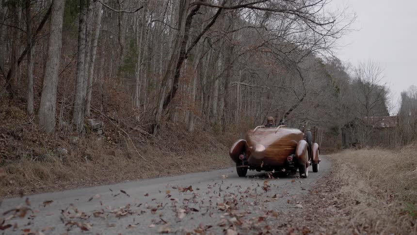 An antique car travels down a forest side road on a winter day