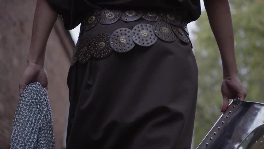 A person is carrying chain mail and a helmet as he walks