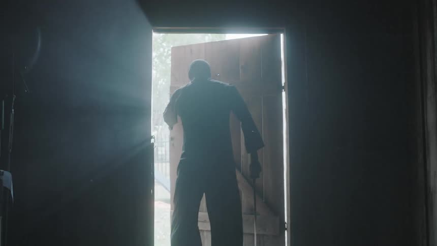 A man walks out of a dark barn into the daylight