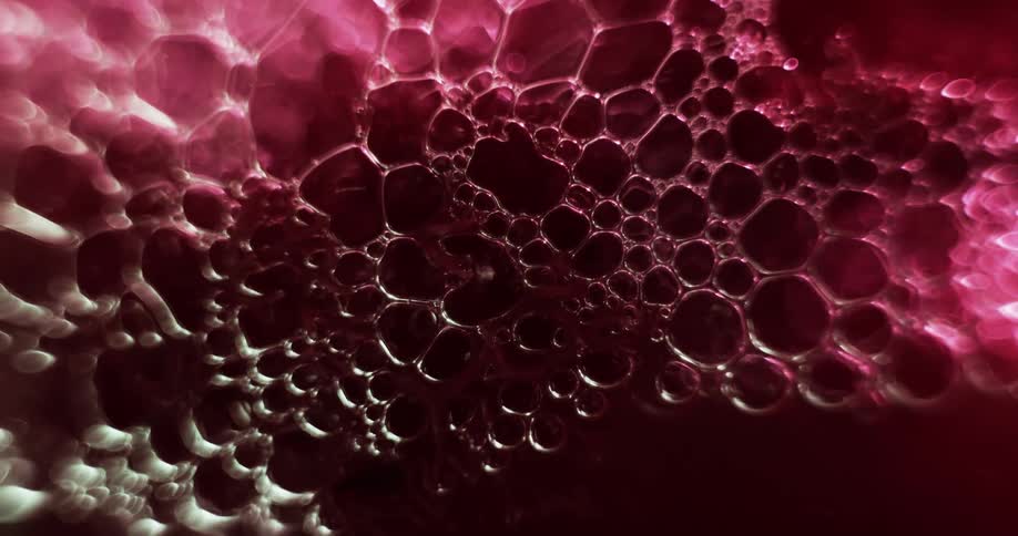 Extreme close up of air bubbles forming on the surface of a liquid under red lights