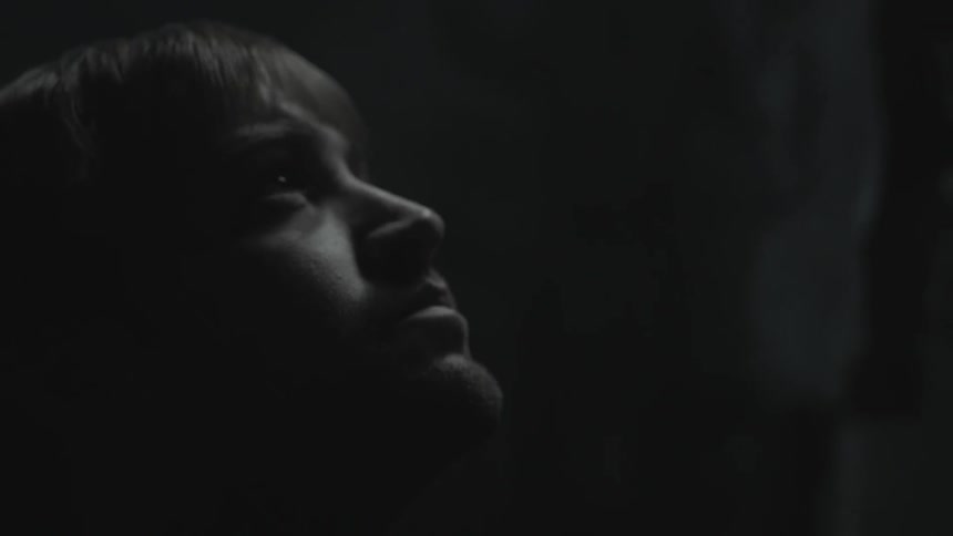 A young man standing in darkness looking up