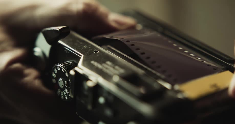 Close up of a man placing a roll of film inside a vintage photography camera