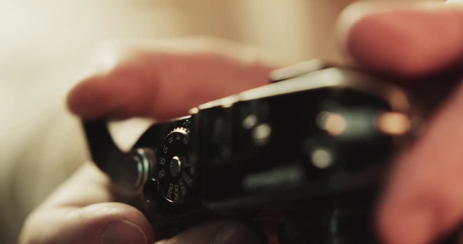 A man flips a switch and turns a knob on a film camera