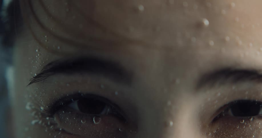 An extreme up close of a eyes on a face underwater with bubbles on it