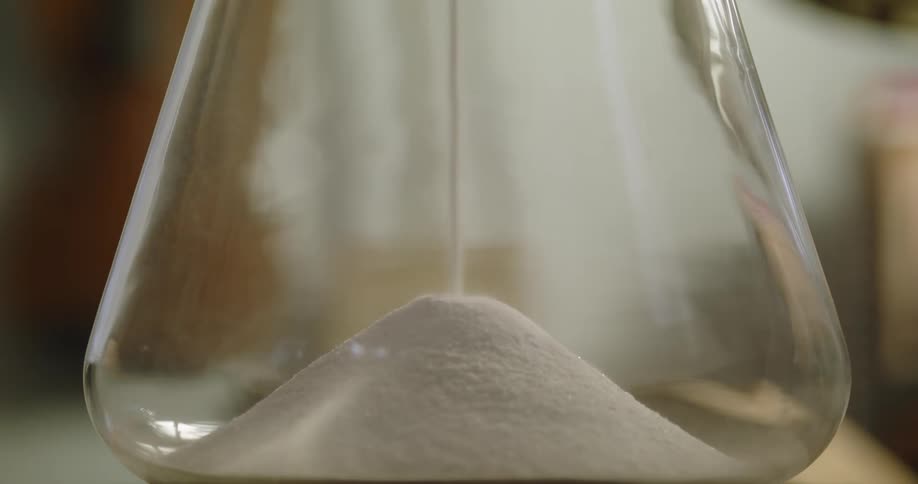White sand is falling to the bottom of an hourglass as it sits on a table