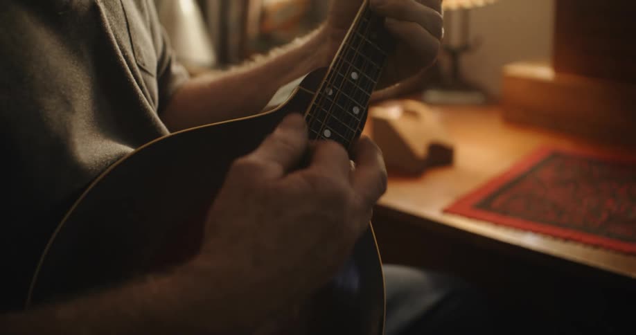A man strumming on a black guitar sitting next to a desk