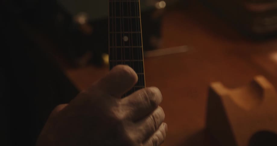 A man is tuning a small guitar while indoors