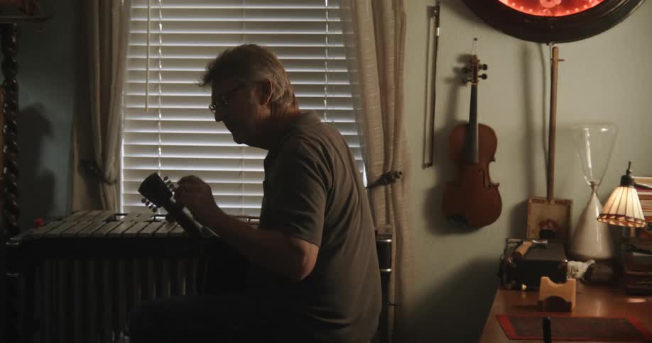An older white man is playing music inside of his home
