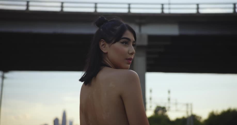 Woman in low cut back dress looks over her shoulder poses for the camera in front of the bridge
