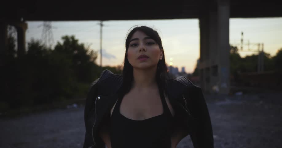 Young woman wearing a leather jacket near a bridge looking at the camera