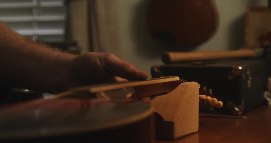 Man carefully placing the neck of a mandolin on a rest over a table