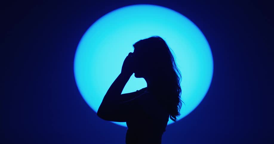 A woman is standing indoors and putting on sunglasses