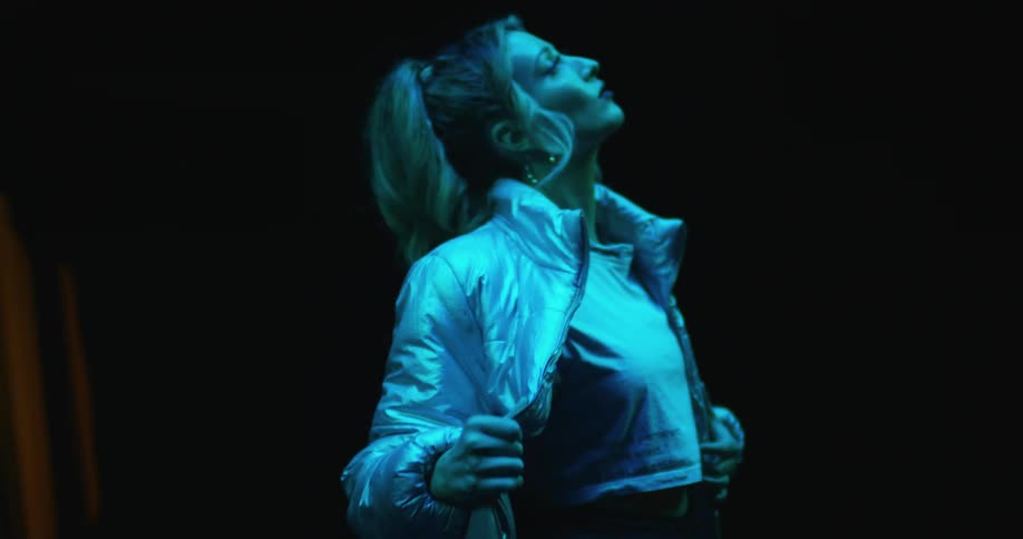 A blonde haired female on a stage taking her coat off and dancing