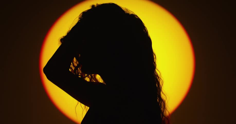 A womans silhouette putting her hands in her hair and lifting up then leaning forward