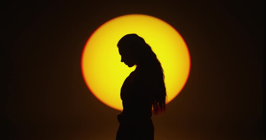 Woman tossing her wavy hair back is silhouetted against the spotlight in the studio