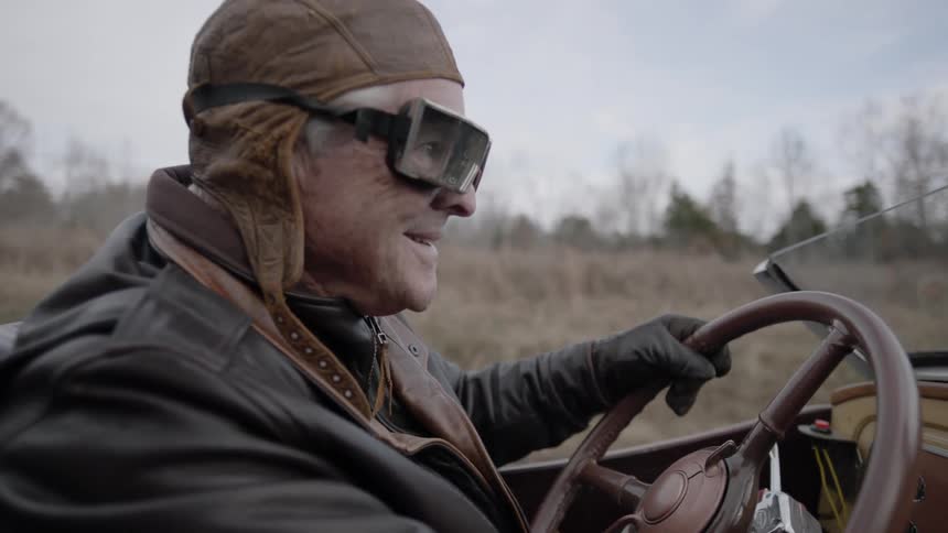 A man in a leather cap drives down the road