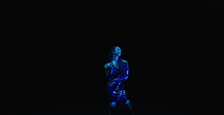 A woman wearing a sparkly dress slowly moving around dancing