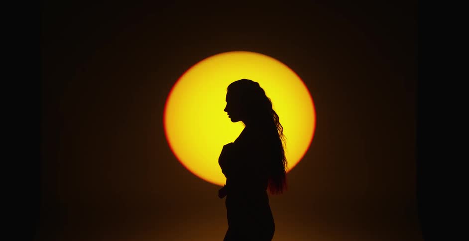 Side view silhouette of a woman with long hair moving in front of a round yellow light