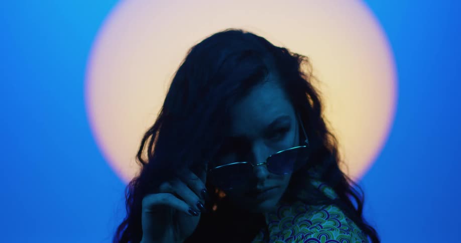 Female model with wavy hair and sunglasses poses for the camera in front of spotlight in the studio