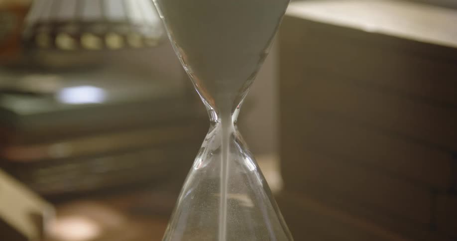 White sand is falling to the bottom of an hourglass as it sits inside a room