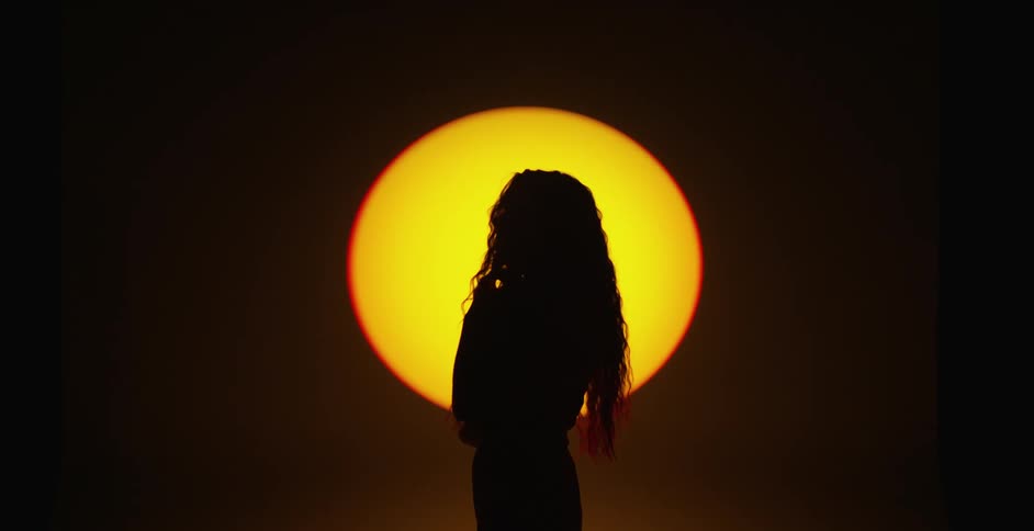 A woman flips her hair by the setting sun