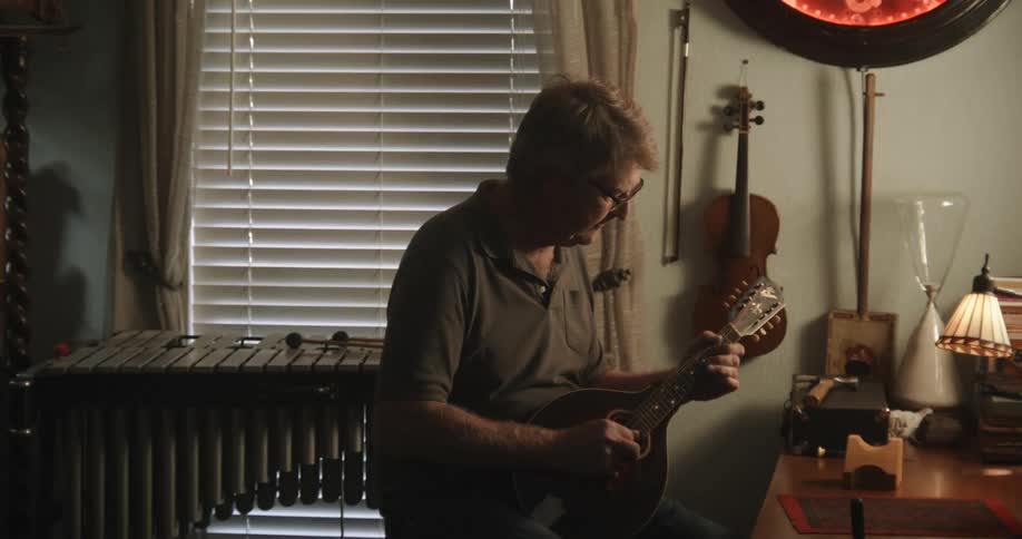 A man plays the ukulele and turns around to use a sound mixer