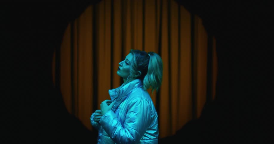 A woman with a blonde pony tail wearing a white coat looking contemplatively with her hand on her cheek