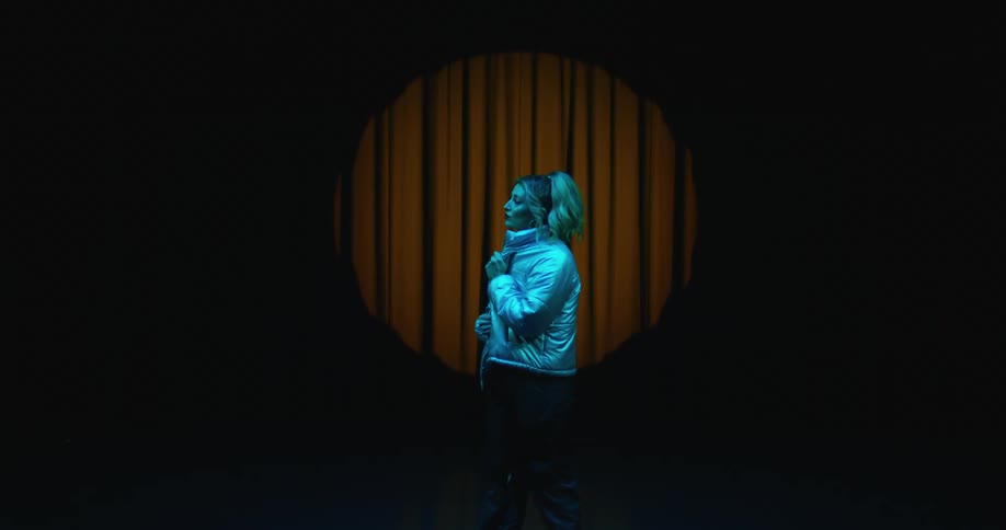 A woman stands on stage in front of a curtain