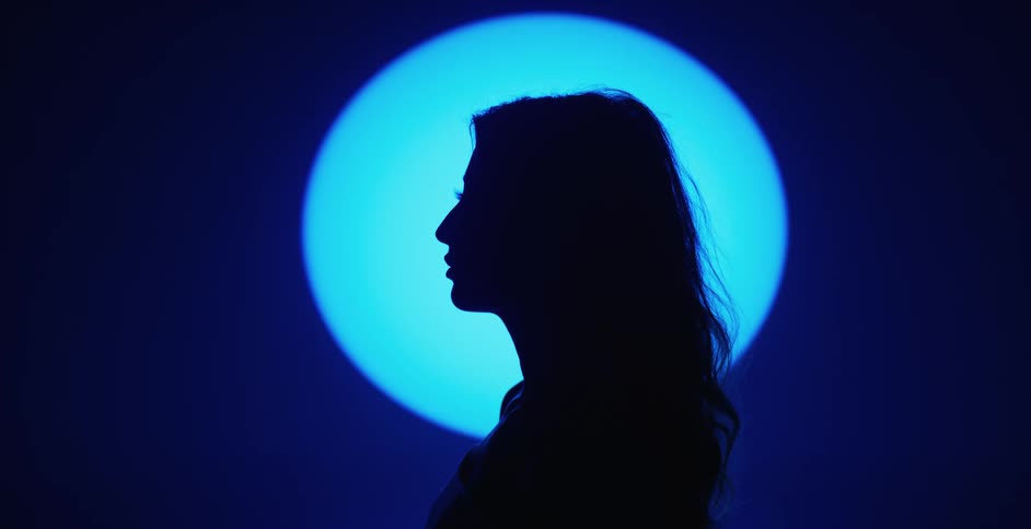 Side profile of female model touching her hair is silhouetted against the spotlight in the studio