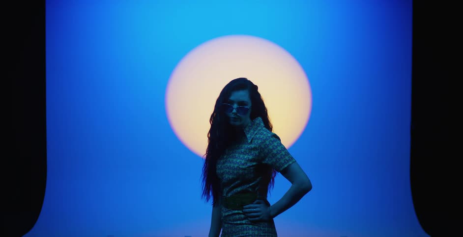 A woman with long dark hair and sunglasses on with her hands on her hips