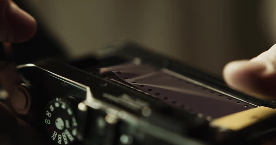 A person placing film in a black camera