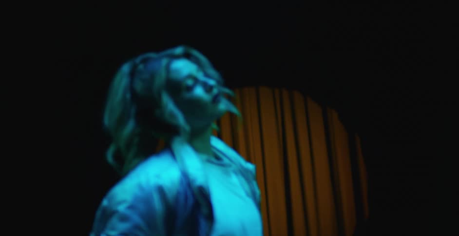 Woman stands posing on stage under blue colored spotlight