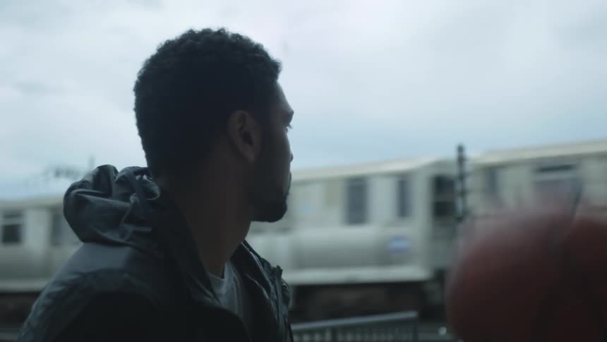 A man watches the train as he tosses a basketball up an down