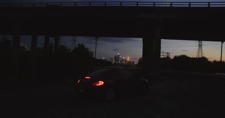 The sun is setting as a car drives under the overpass