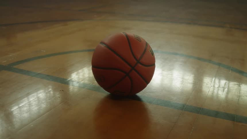 A basketball sits on the floor of an indoor basketball court