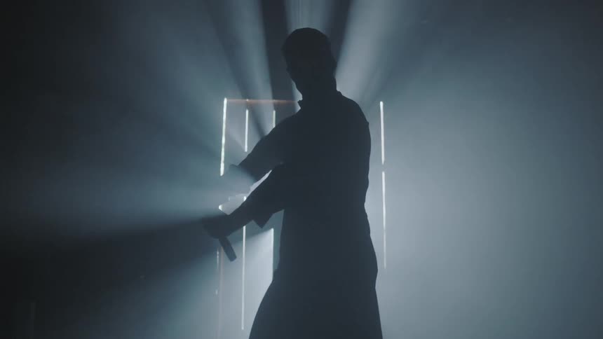 A man brandishes a sword in front of a door with sunlight streaming in