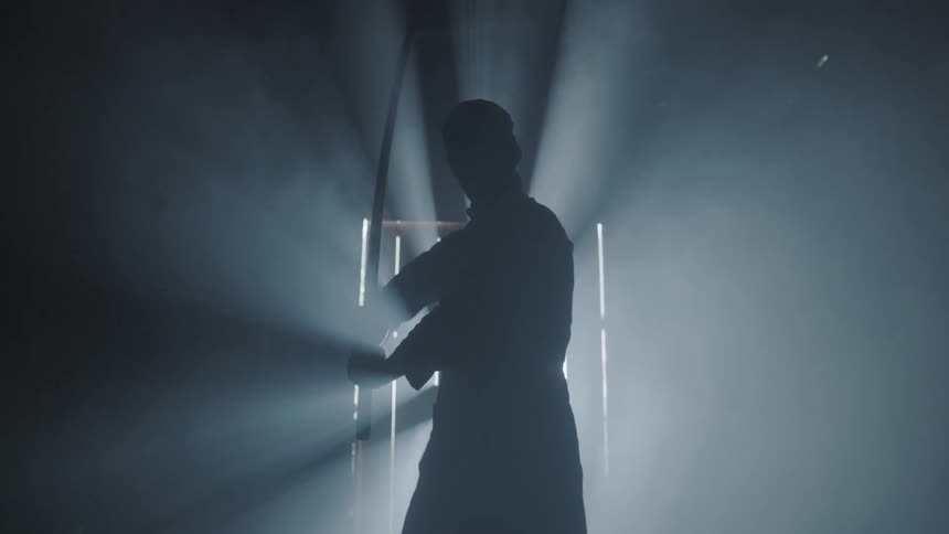 A man is practicing with a sword in a dark room