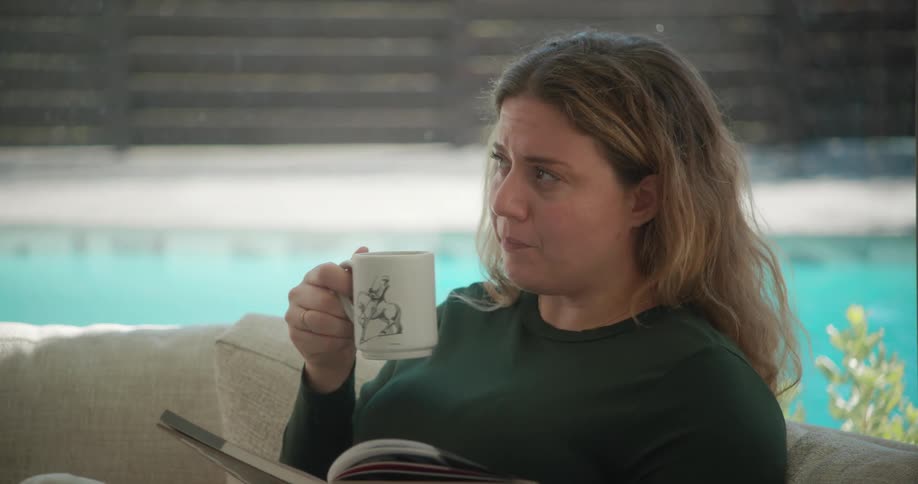 Thoughtful woman sitting on the sofa drinking a cup of coffee and reading a book