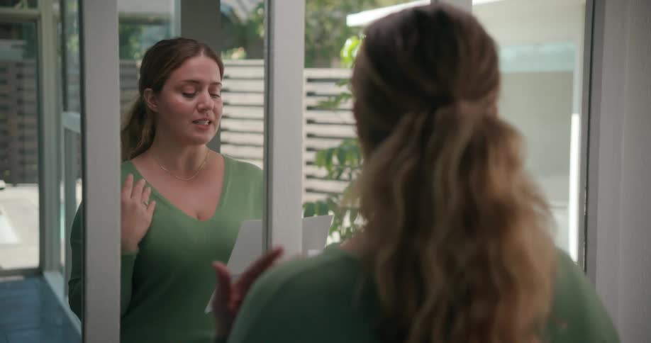 A woman is standing in front of a mirror reading from a sheet of paper
