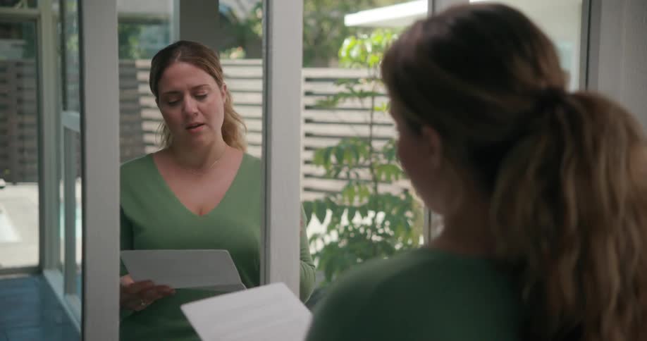 A woman practices a speech while standing at a window in her home