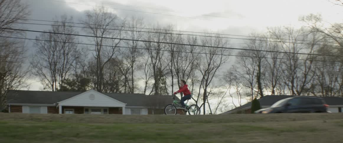 A boy rides his bicycle in a neighborhood on an overcast day