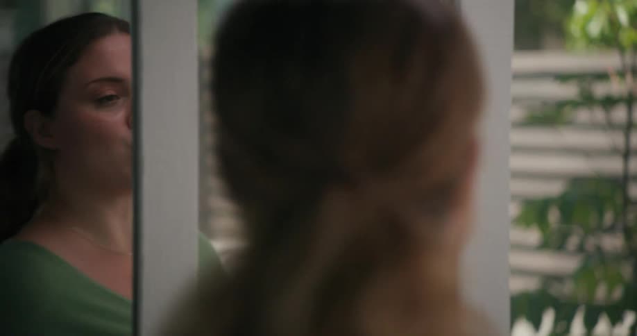 Woman with brown ponytail and green sweater practices in front of the mirror