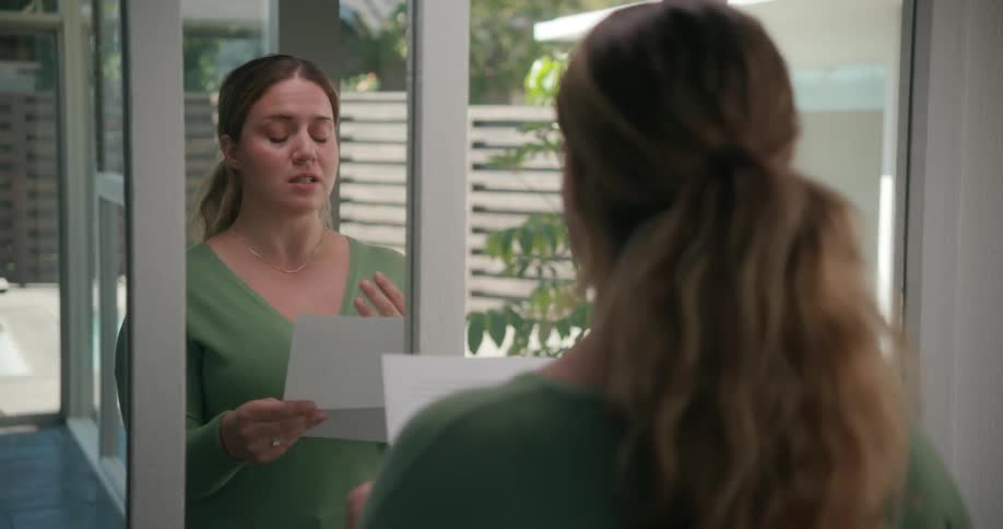 A woman stands at home and reads a paper as she practices a speech