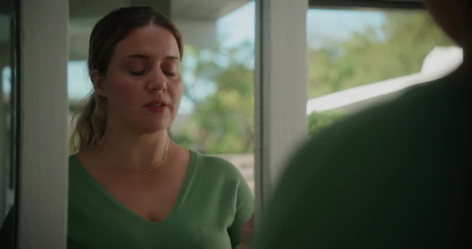 A woman looks in the mirror and reads something off of a piece of paper she is holding in her hand