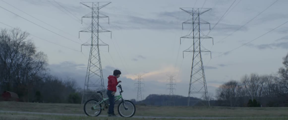 A child riding a green bike stops on the road