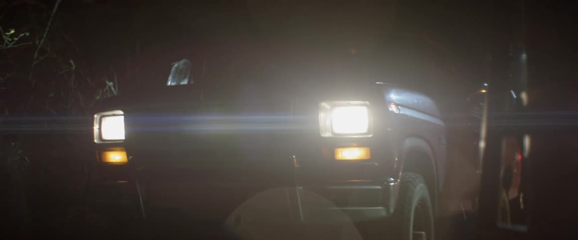 People with flashlights get out of a red pick up truck on a rainy night