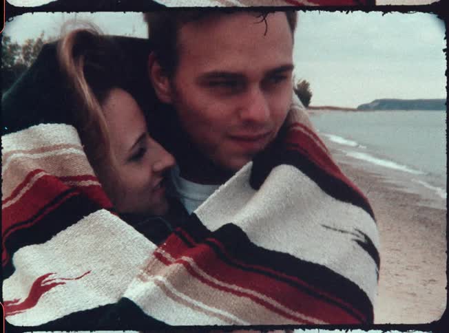 A man and woman on a date kiss while bundled in a blanket on the beach