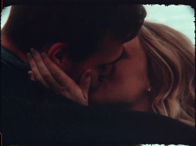 A man and woman kiss by the shore